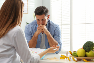 Young nutritionist consulting patient at table in clinic