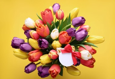 Photo of Bouquet of beautiful colorful tulips with blank card on yellow background, top view. Birthday celebration