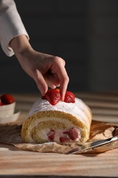 Woman decorating delicious cake roll with strawberries at table, closeup