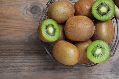Photo of Metal basket with cut and whole fresh kiwis on wooden table, top view. Space for text
