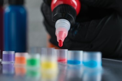 Tattoo artist dripping red tattoo ink into cap on table, closeup