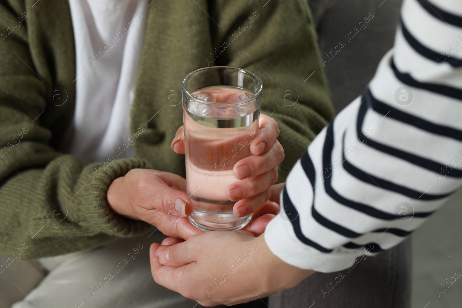 Photo of Caregiver giving water to elderly woman at home, closeup