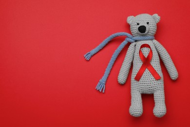 Cute knitted toy bear with ribbon on red background, top view and space for text. AIDS disease awareness