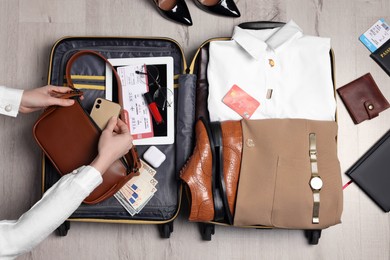 Woman packing suitcase for business trip on wooden floor, top view