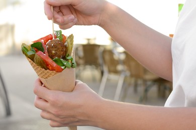 Photo of Woman eating wafer with falafel and vegetables outdoors, closeup. Street food
