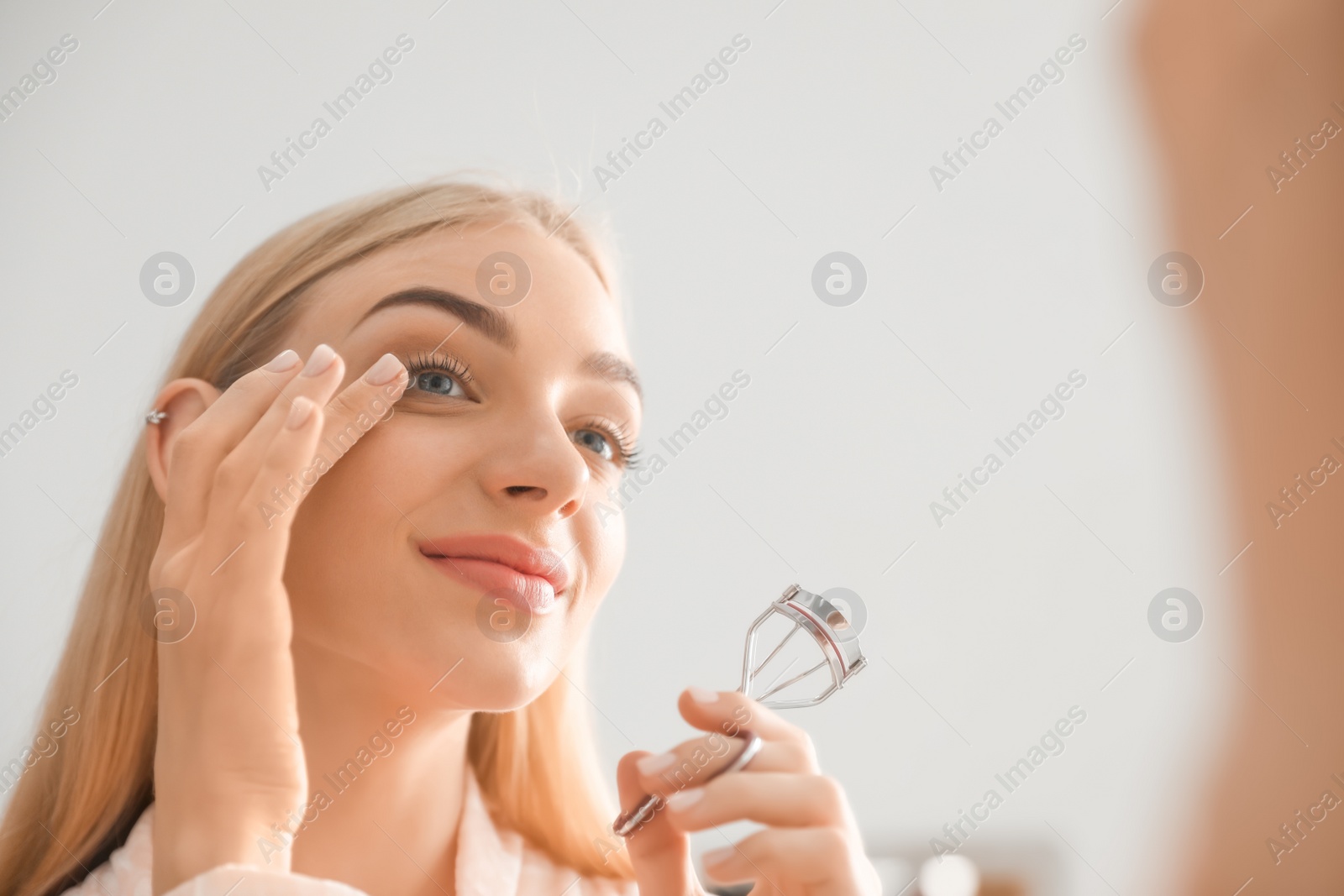 Photo of Attractive young woman curling her eyelashes indoors