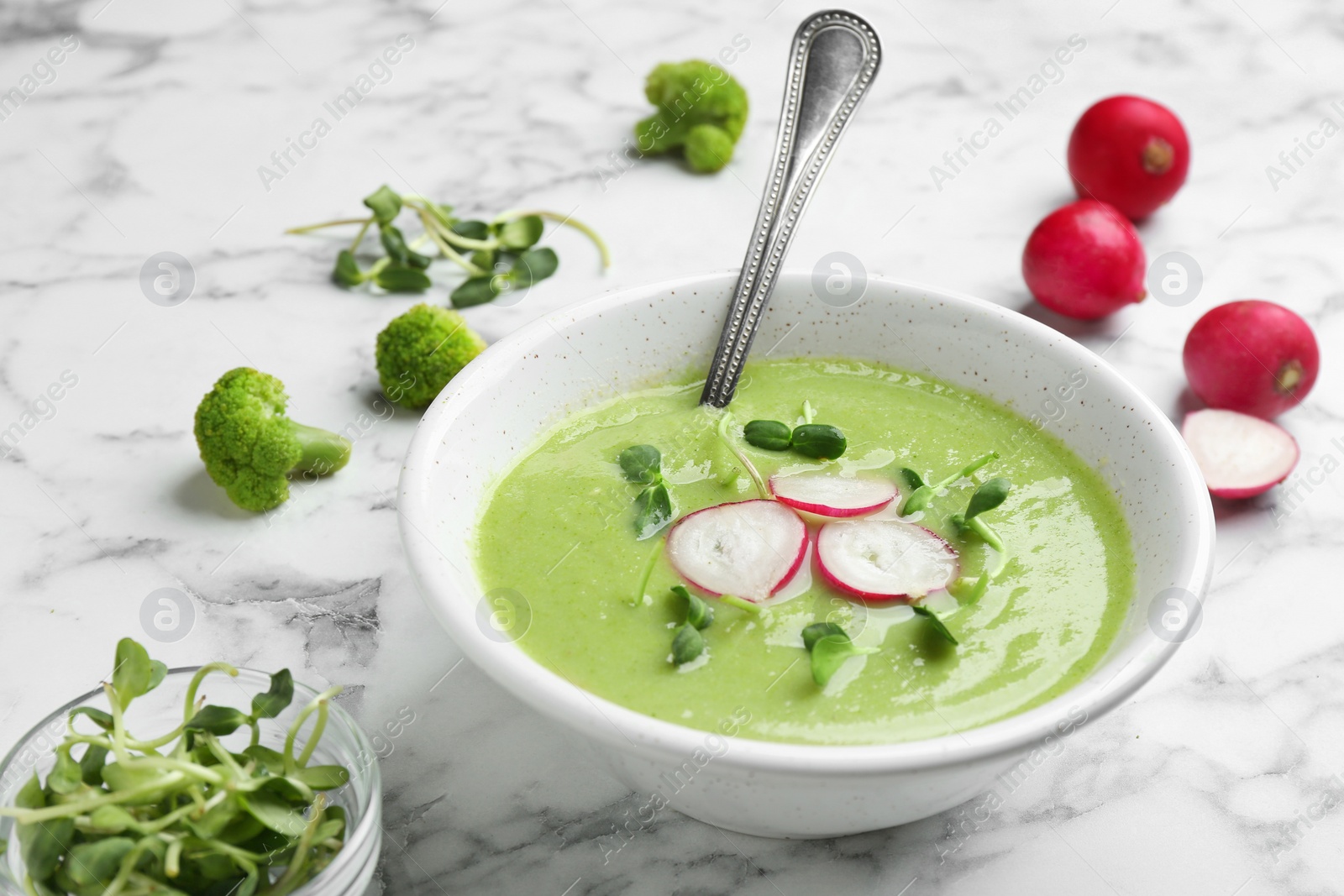 Photo of Bowl of broccoli cream soup with radish and microgreens served on white marble table