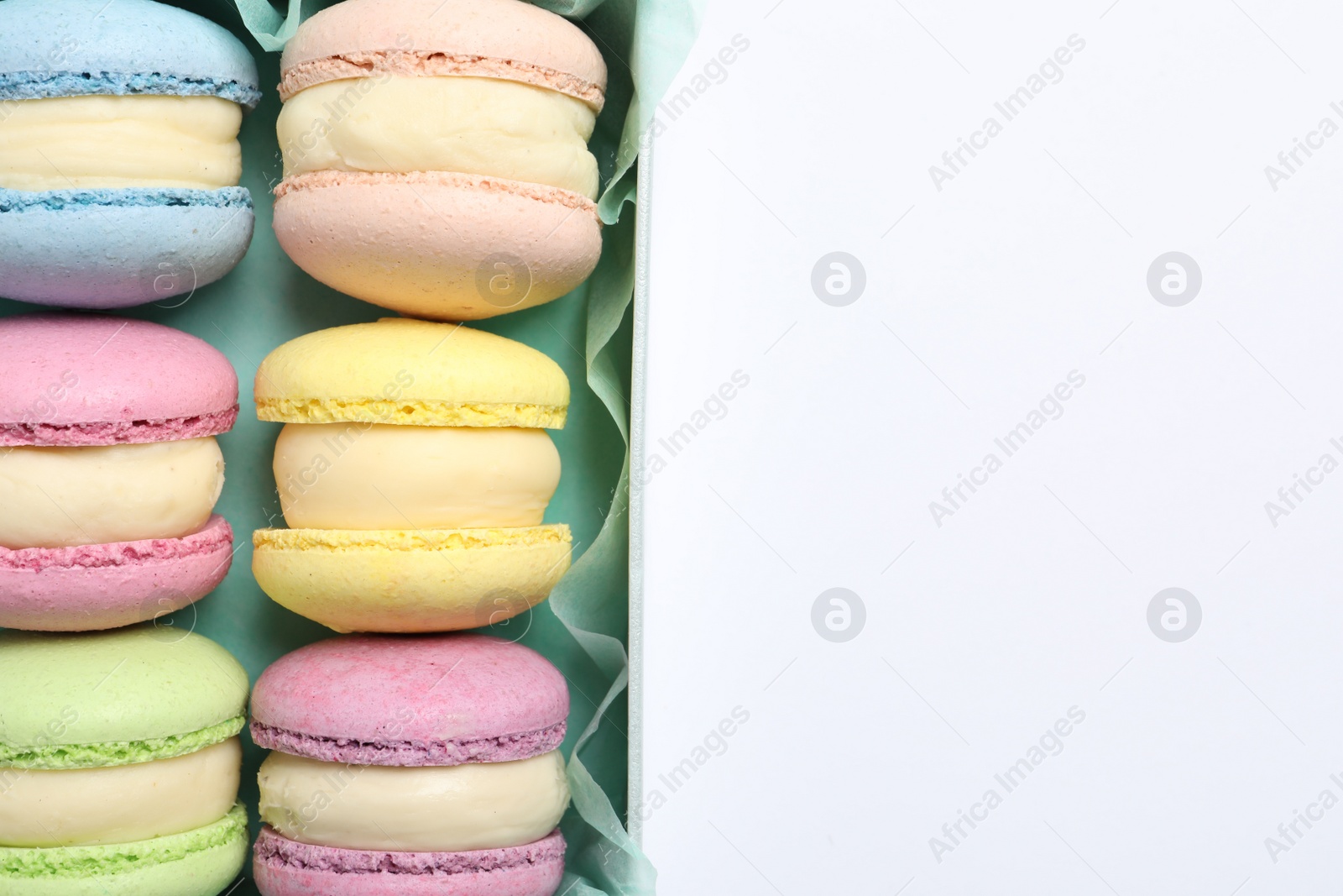 Photo of Many delicious colorful macarons in box on white background, top view