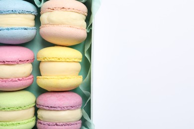 Many delicious colorful macarons in box on white background, top view