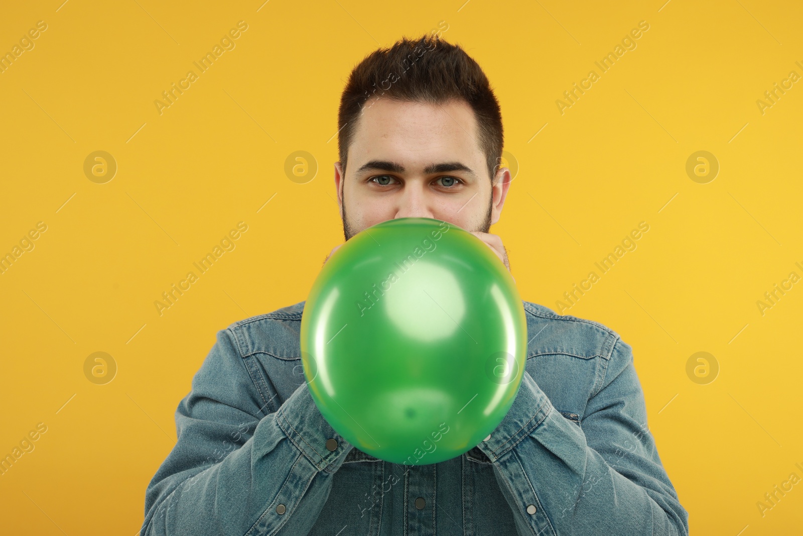 Photo of Man inflating bright balloon on yellow background