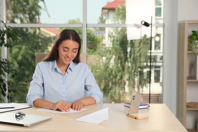 Photo of Beautiful young woman making paper plane at desk in office
