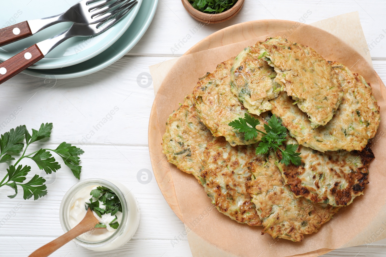 Photo of Delicious zucchini fritters served on white wooden table, flat lay