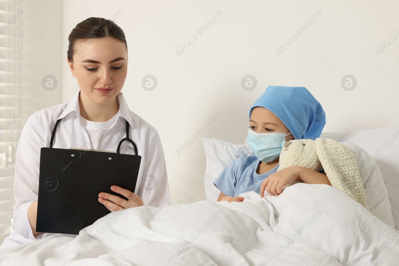 Photo of Childhood cancer. Doctor with clipboard and little patient with toy bunny in hospital