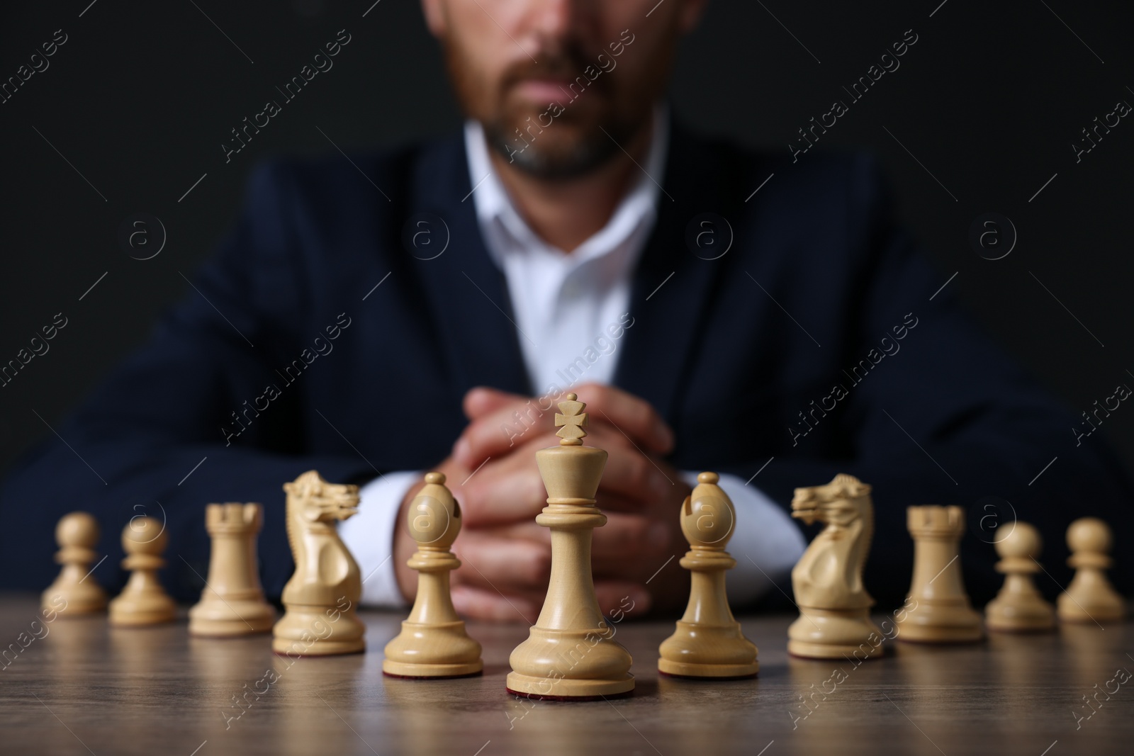 Photo of Man with chess pieces at wooden table against dark background, closeup