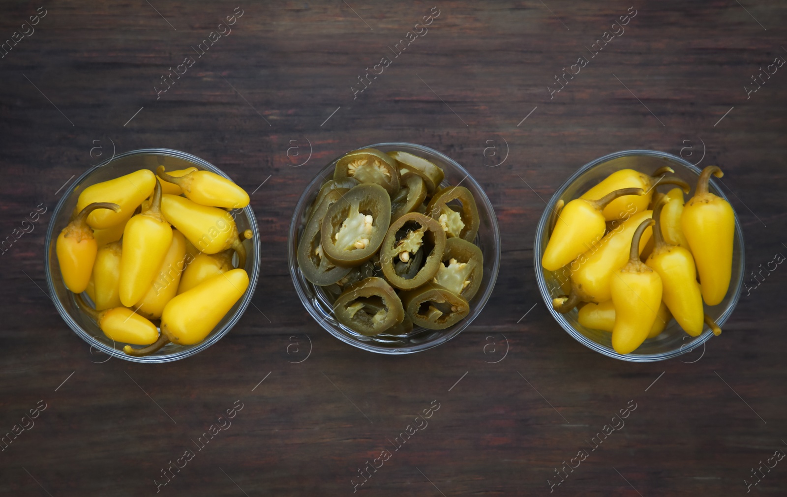 Photo of Pickled green and yellow jalapeno peppers on wooden table, flat lay