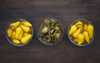 Pickled green and yellow jalapeno peppers on wooden table, flat lay