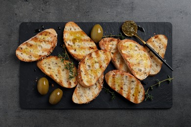 Tasty bruschettas with oil, thyme and olives on grey table, top view