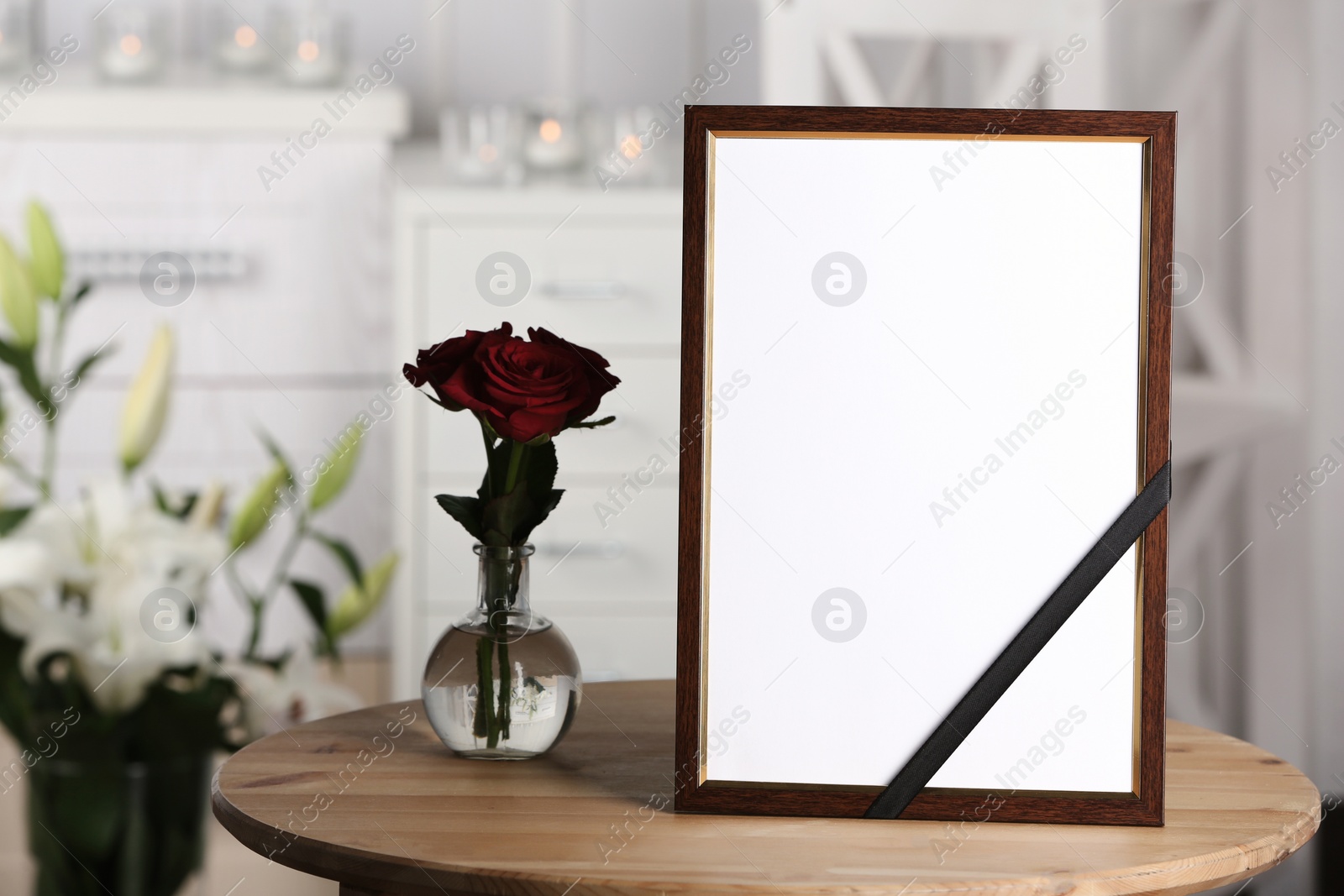 Photo of Funeral photo frame with black ribbon and roses on table, indoors