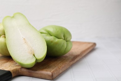 Photo of Cut and whole chayote on white tiled table, closeup