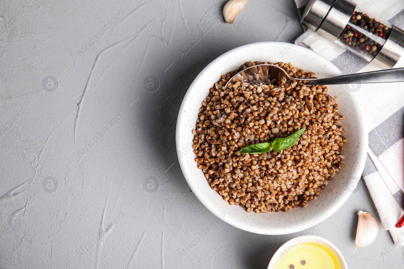 Photo of Flat lay composition with bowl of buckwheat porridge served on grey table. Space for text