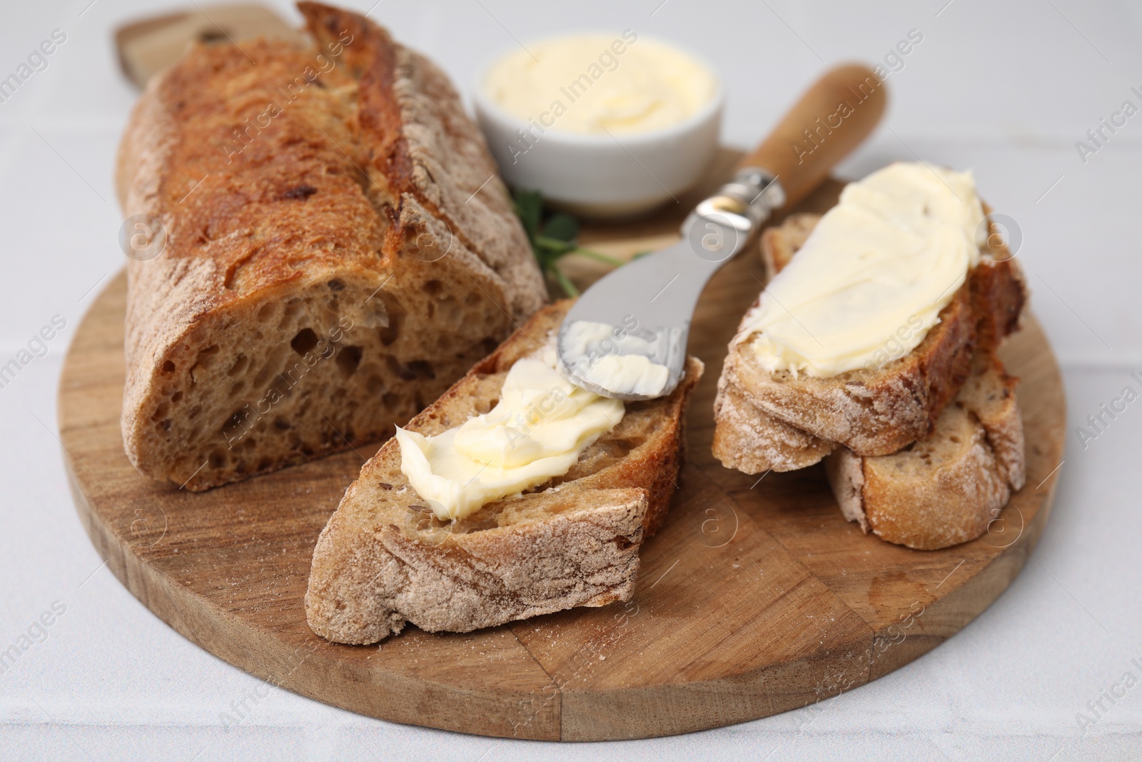 Photo of Tasty bread with butter and knife on white tiled table, closeup