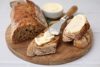 Tasty bread with butter and knife on white tiled table, closeup