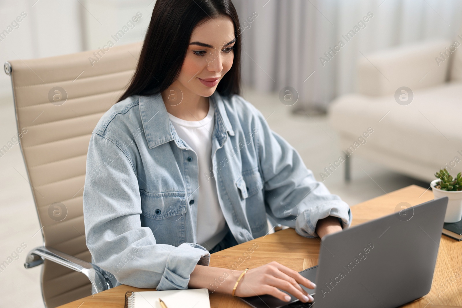 Photo of Young woman watching webinar at table in room