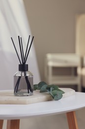 Photo of Aromatic reed air freshener and eucalyptus branch on white table in room, space for text