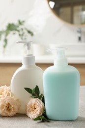 Photo of Dispensers of liquid soap and roses on light grey table in bathroom