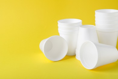 Photo of White styrofoam cups on yellow background, space for text