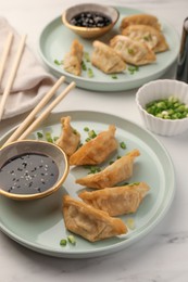 Photo of Delicious gyoza (asian dumplings) with soy sauce and green onions on white table