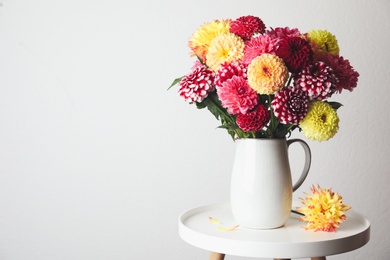 Photo of Bouquet of beautiful dahlia flowers on table near white wall. Space for text