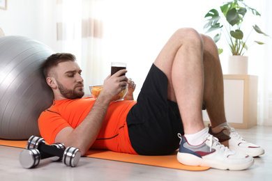 Photo of Lazy young man eating junk food on yoga mat at home
