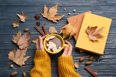 Woman with cup of hot drink at blue wooden table, top view. Cozy autumn atmosphere