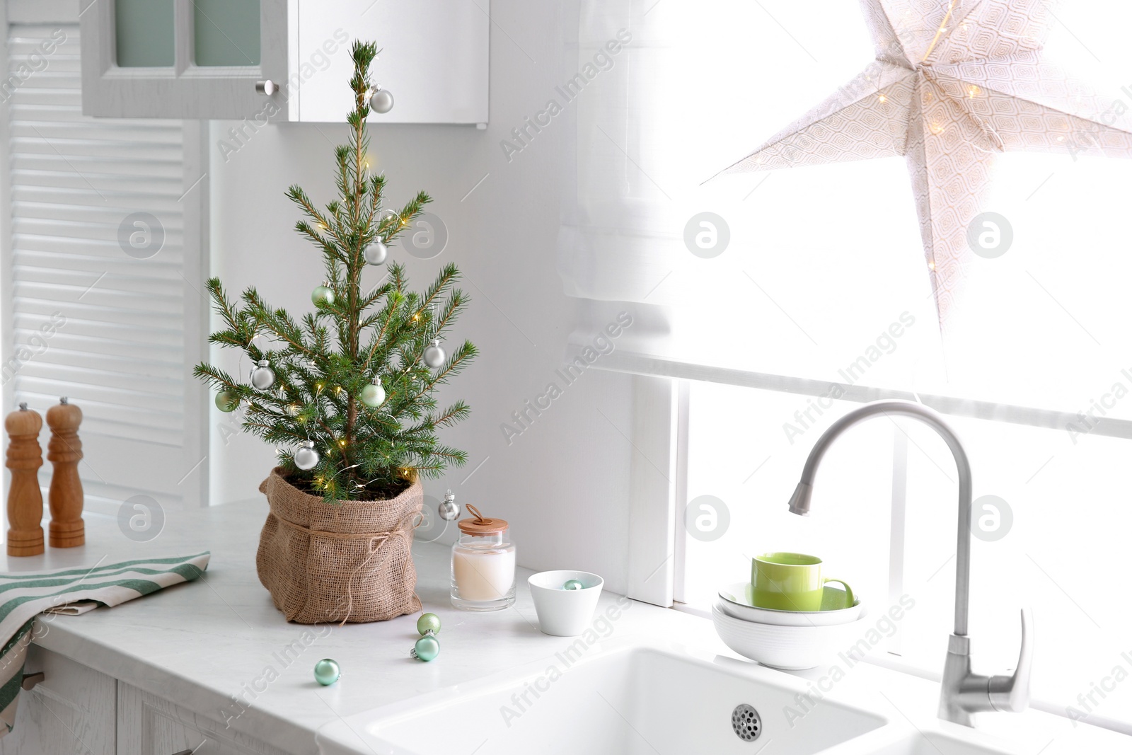 Photo of Small Christmas tree decorated with baubles and festive lights in kitchen