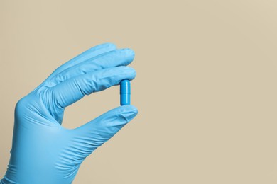 Doctor holding pill on beige background, closeup. Space for text