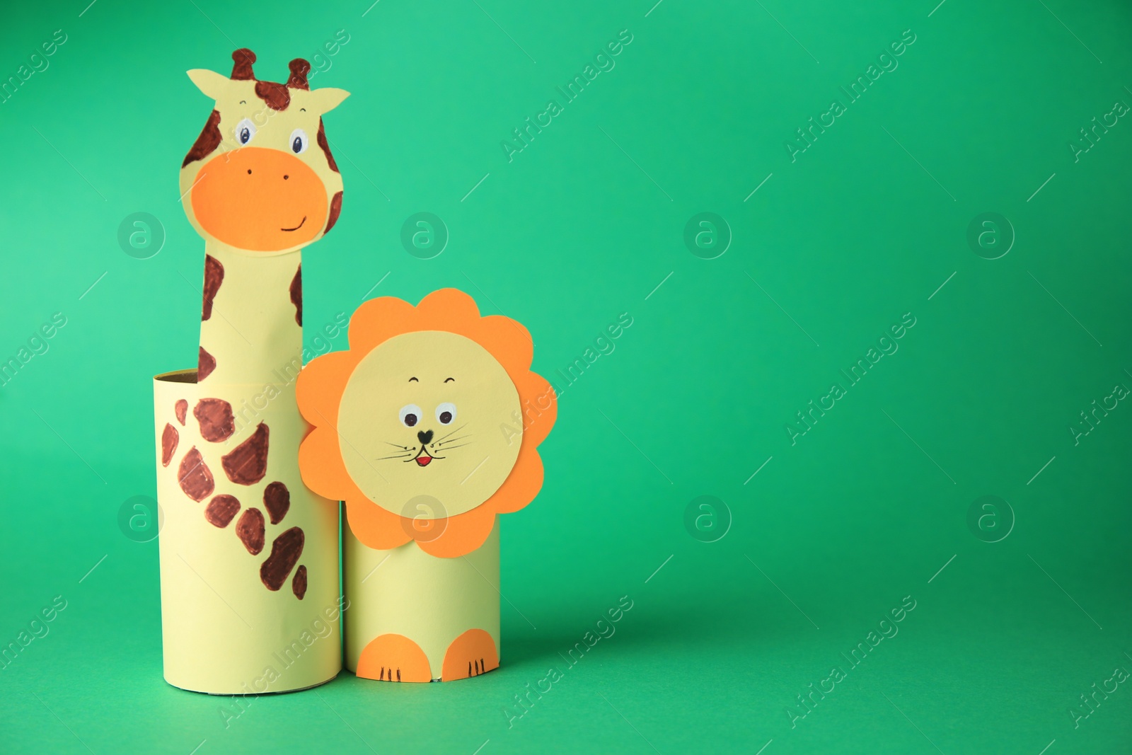 Photo of Toy giraffe and lion made from toilet paper hubs on green background, space for text. Children's handmade ideas