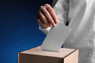 Photo of Woman putting her vote into ballot box on dark blue background, closeup