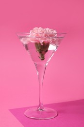 Photo of Martini glass with water and beautiful carnation flower on pink background