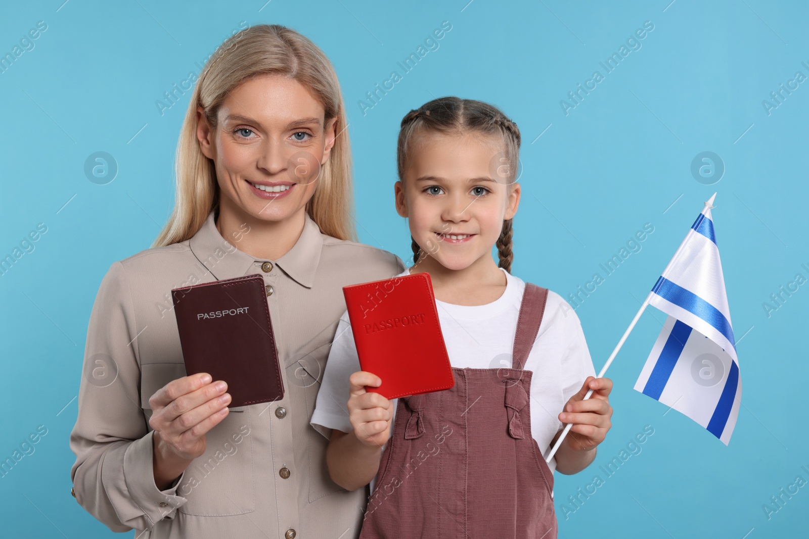 Photo of Immigration. Happy woman with her daughter holding passports and flag of Israel on light blue background