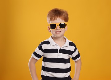 Cute little boy with sunglasses on yellow background