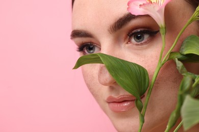 Photo of Beautiful woman with fake freckles and flower on pink background, closeup. Space for text