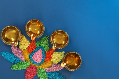Photo of Diwali celebration. Diya lamps and colorful rangoli on blue background, flat lay. Space for text
