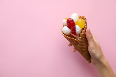 Woman holding wafer cone with delicious lollipop candies on pink background, top view. Space for text