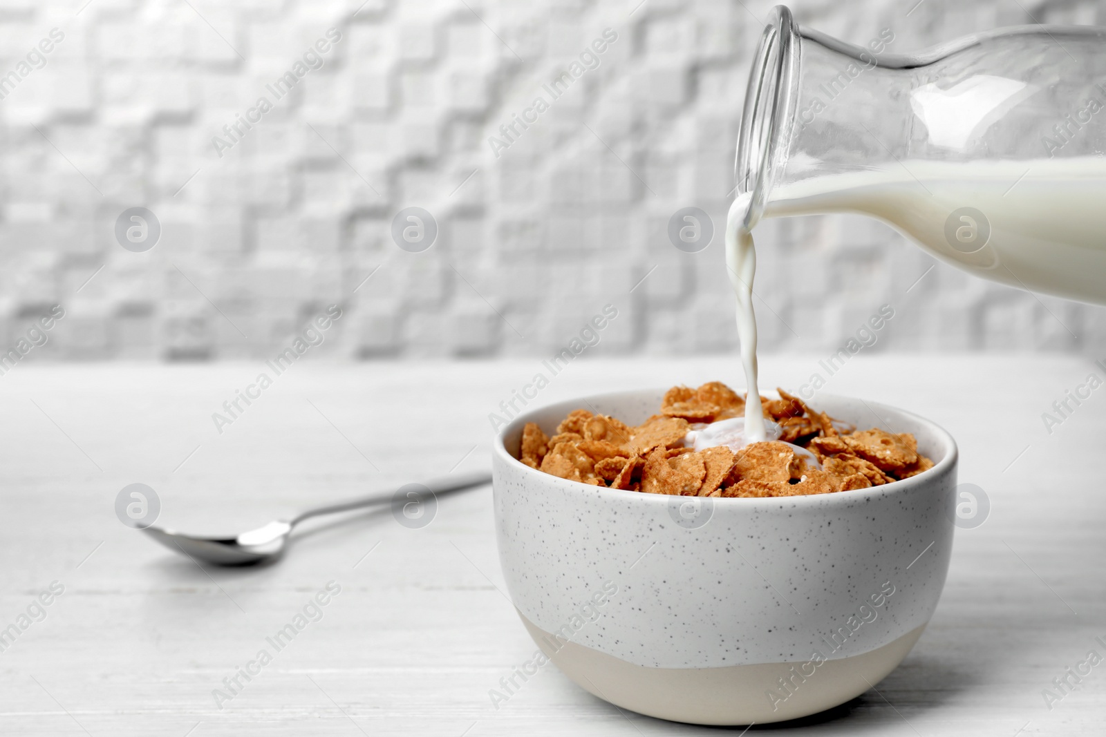 Photo of Pouring milk into bowl with cornflakes on light table. Whole grain cereal for breakfast