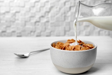 Photo of Pouring milk into bowl with cornflakes on light table. Whole grain cereal for breakfast