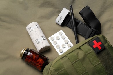 Military first aid kit, tourniquet, pills and elastic bandage on khaki fabric, flat lay