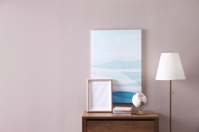 Photo of Wooden chest of drawers with globe, books and empty frame near beige wall in room, space for text. Interior design