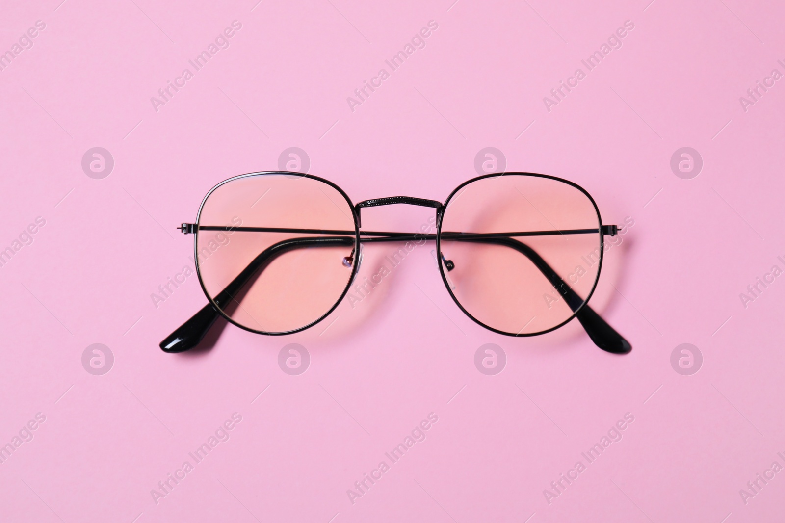 Photo of Stylish pair of glasses with black frame on pink background, top view