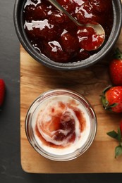 Photo of Tasty yoghurt with jam and strawberries on black table, top view